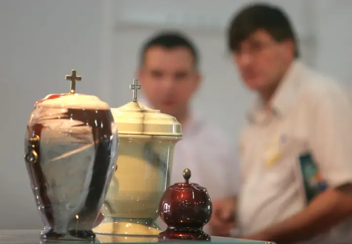 Trzy urny pogrzebowe z krzyżami, w tle niewyraźne postacie. Temat kremacji budzi dyskusje, nawet wśród hierarchów Kościoła, jak papież o kremacji.