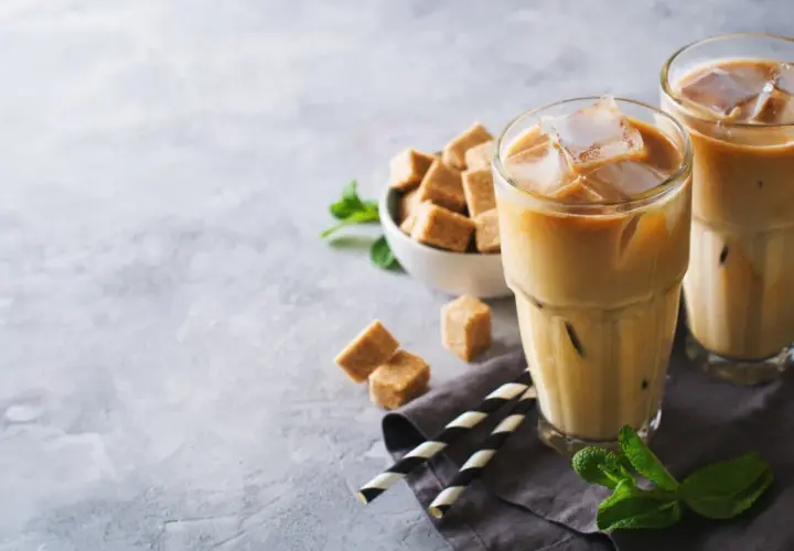 Dwa orzeźwiające freddo espresso z lodem, kostki brązowego cukru i listki mięty na szarym tle. Idealne na upalny dzień.