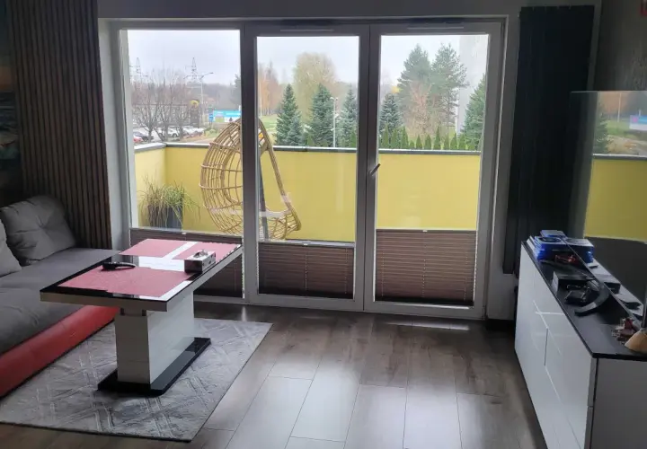 Wygodny salon z widokiem na atrium Radogoszcz. Na tarasie huśtawka i zieleń.