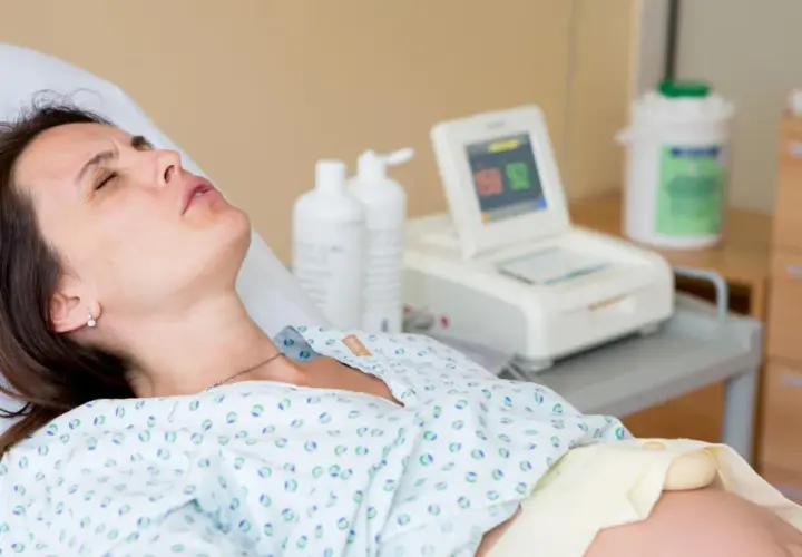 Kobieta w szpitalnym łóżku, monitor KTG, butelki z płynem. Badanie może wykluczyć obecność bakterii Streptococcus agalactiae.