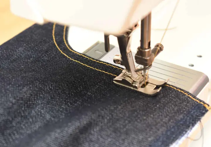 Close-up of a sewing machine stitching dark denim with yellow thread. Perfect sewing machine settings for denim are key for strong seams.