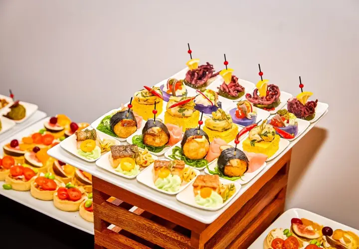 Elegancki catering urodzinowy Warszawa: kolorowe przekąski, sushi, tartaletki i owoce morza na białych talerzykach.