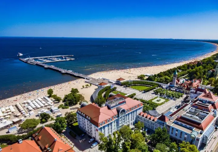 Widok na fajny hotel nad morzem, z plażą pełną ludzi i molo.