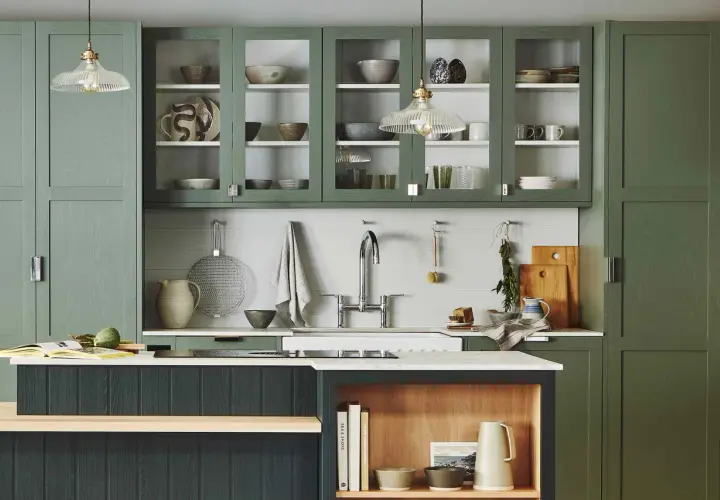 Stylish glass cabinet decor ideas in a modern kitchen with green cabinetry, showcasing ceramic bowls, plates, and glassware.
