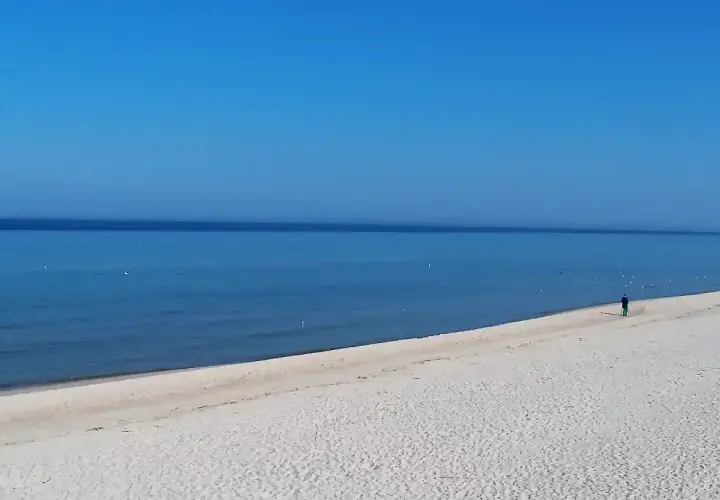 Grzybowo nadmorskie: zejście na plażę. Dwie osoby spacerują po piaszczystej plaży, morze i błękitne niebo.
