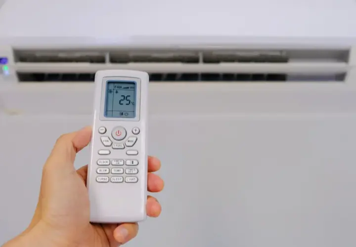 Mano sujetando control remoto de aire acondicionado, mostrando el símbolo deshumidificador aire acondicionado en pantalla.