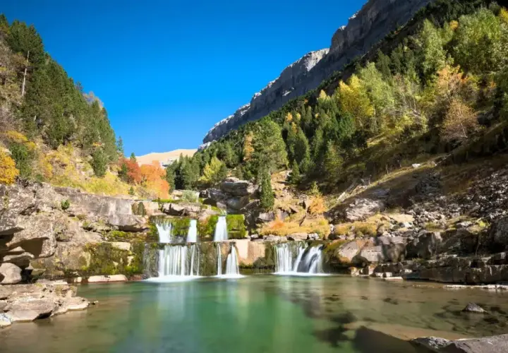 Cascada en un valle montañoso con árboles otoñales. Un lugar perfecto para rutas de senderismo inolvidables.
