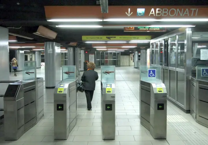 Ingresso della metropolitana di Roma con tornelli ATAC. Una donna attraversa i varchi per accedere ai binari.