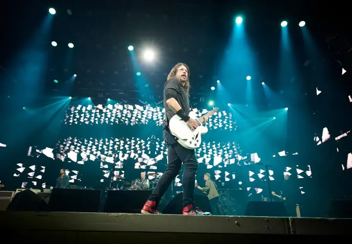 Dave Grohl z Foo Fighters gra na gitarze podczas koncertu, oświetlony niebieskimi światłami. Chce pokazać, jak grać.