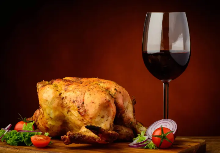 Pollo arrosto dorato con contorno di verdure fresche e un bicchiere di vino rosso, perfetto vino da abbinare al pollo.
