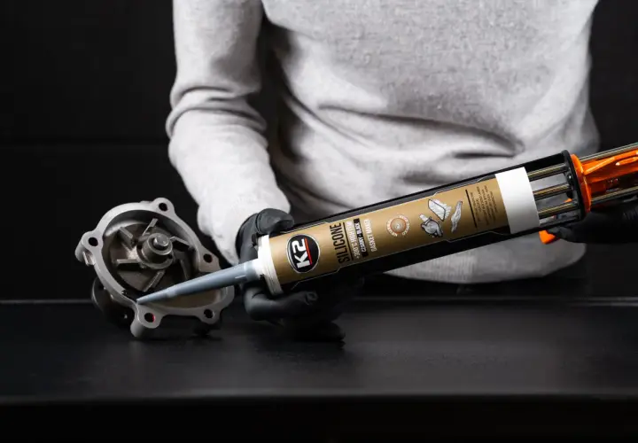 Rękawiczki i pistolet z czarnym silikonem K2. Aplikacja uszczelniacza na element pompy wodnej. Dowiedz się, jak długo schnie silikon.