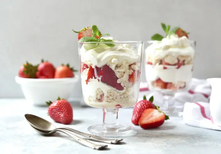 Pyszny Eton Mess z truskawkami i bitą śmietaną w kieliszkach, ozdobiony miętą.