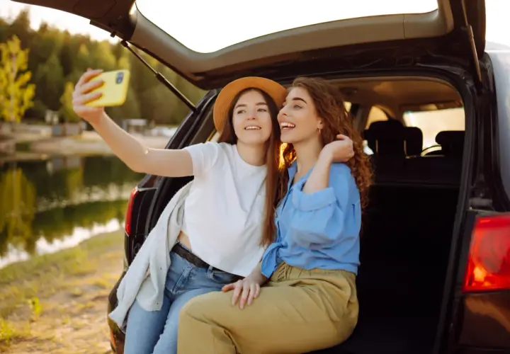 Dwie przyjaciółki robią sobie selfie przy samochodzie nad jeziorem. Idealny weekend z przyjaciółką!