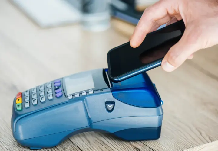 Dłoń zbliża smartfon do terminala płatniczego, realizując szybki booking paypo.