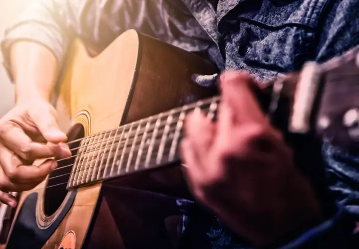 Ręce grające na gitarze akustycznej. Dowiedz się, jak samemu nauczyć się grać na gitarze, ćwicząc akordy i rytm.