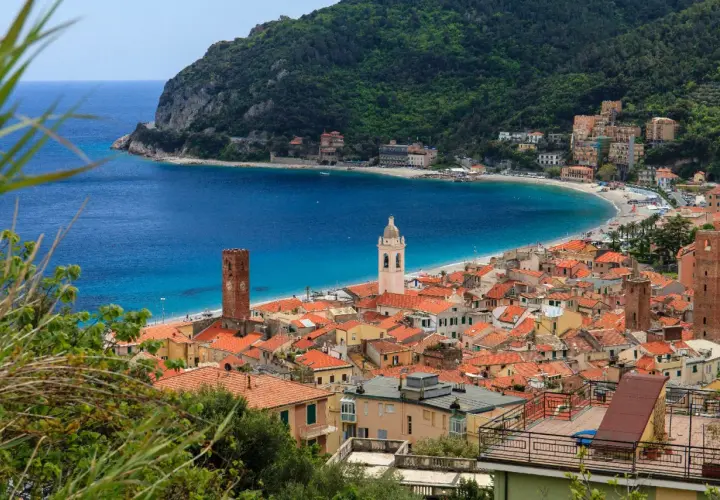 Vue d'un village pittoresque sur la côte de l'Italian Riviera, avec des maisons aux toits rouges, une plage de sable et une mer bleue étincelante.