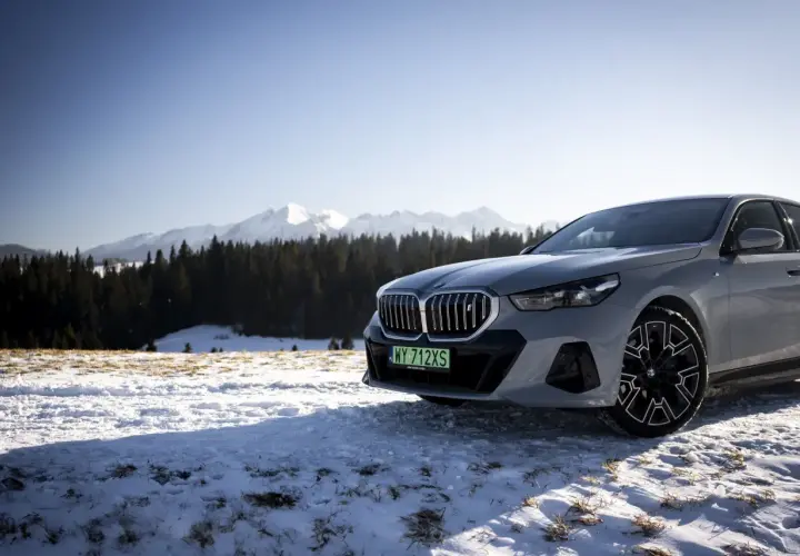 Szare BMW i5 na tle ośnieżonych gór i lasu.