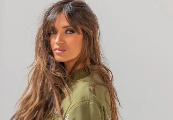 Mujer con cabello castaño largo y ondulado, con flequillo cortina que enmarca su rostro.