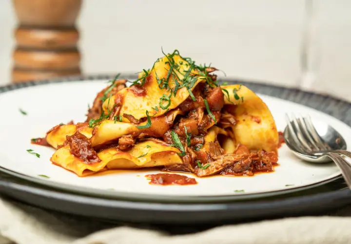 Herzhaftes Pasta Ragu mit breiten Nudeln, übergossen mit einer reichhaltigen Fleischsauce und garniert mit frischen Kräutern.