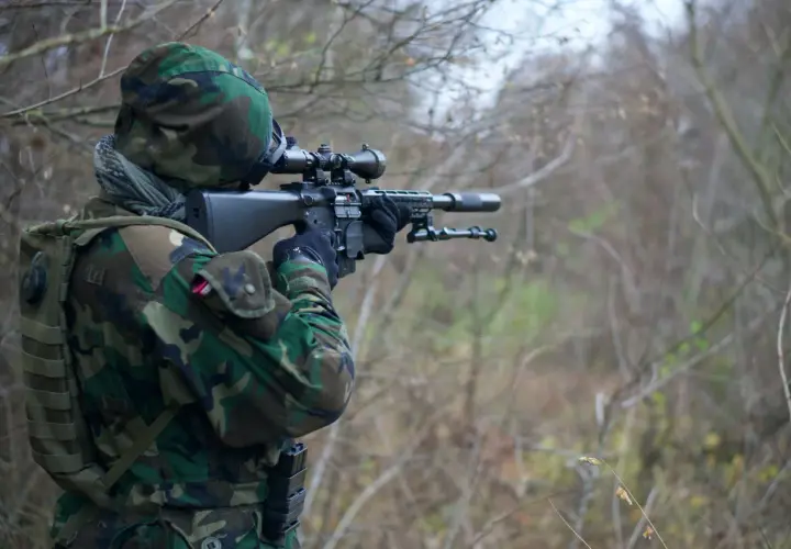 Żołnierz w kamuflażu celuje z karabinu snajperskiego. Widać lunetę, przez którą obserwuje cel, a zjawisko paralaksy w lunecie jest kluczowe dla precyzyjnego strzału.