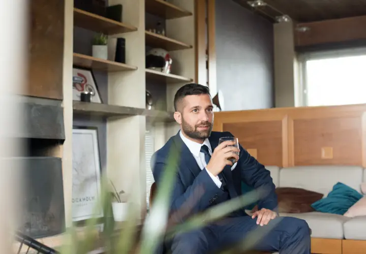 Elegancki mężczyzna w garniturze, z drinkiem w dłoni, emanuje spokojem i pewnością siebie w towarzystwie.