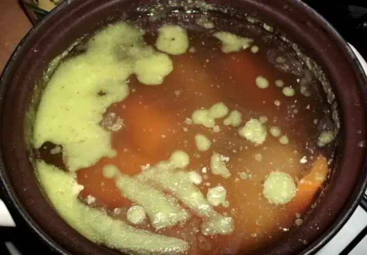 Gęsta, zielona piana na powierzchni aromatycznej zupy na rosole. Widać kawałki warzyw i mięsa.