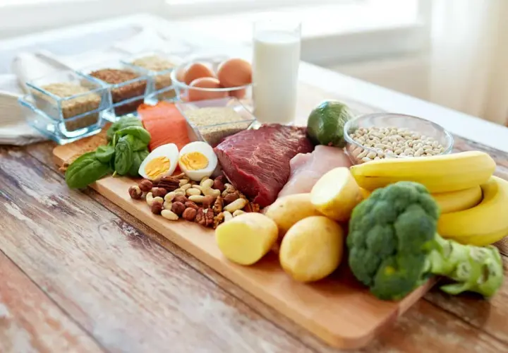 Deska z różnorodnymi produktami spożywczymi: mięso, ryba, jajka, orzechy, warzywa, owoce, mleko i ziarna.
