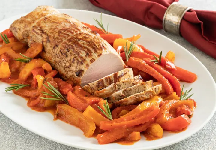 Arrosto di vitello in pentola con peperoni e carote, guarnito con rosmarino. Un piatto succulento e colorato.