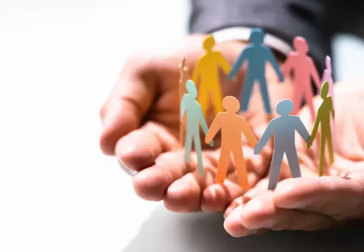 Hands cradle colorful paper people, symbolizing the benefits of equality, diversity, and inclusion in the workplace.