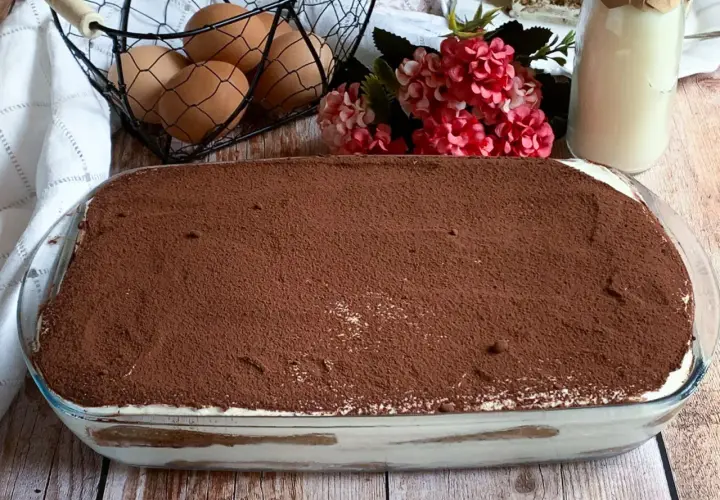 Tiramisù fatto in casa, una ricetta con panna che promette golosità. Uova fresche e cacao in polvere completano la scena.