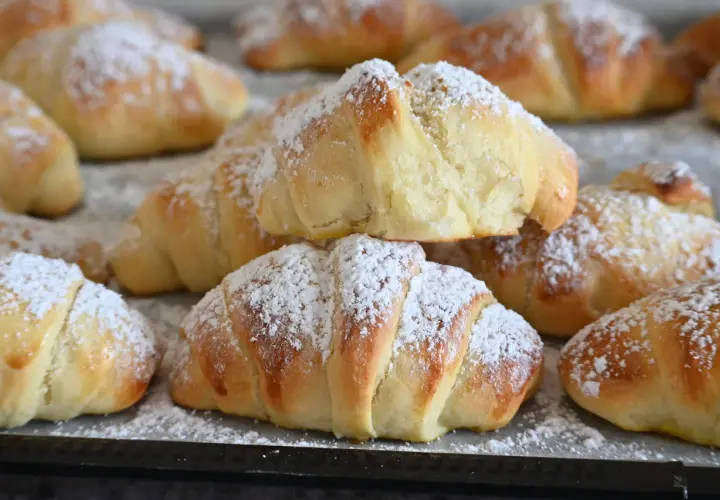 Brioches fatte in casa, dorate e soffici, cosparse di zucchero a velo. Un dolce profumo che invita a gustare la colazione.