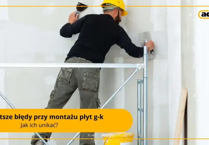 Budowlaniec w żółtym kasku i roboczych spodniach na rusztowaniu wygładza ścianę gładzią. Unikaj błędów przy montażu płyt g-k, jak przy nitowaniu.