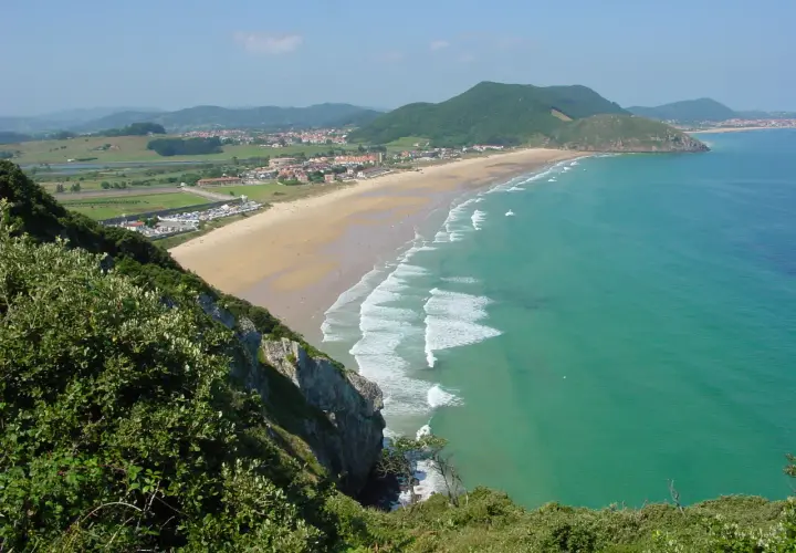 Vista panorámica de la playa de Berria, con arena dorada, aguas turquesas y colinas verdes al fondo.