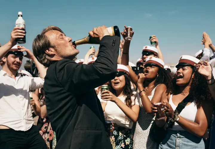 Mads Mikkelsen dricker ur en champagneflaska, omgiven av glada studenter med studentmössor. En runda till recension av firandet.