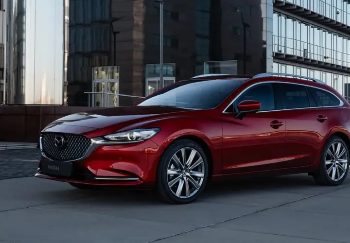 Czerwona Mazda 6 kombi na tle nowoczesnego budynku. Poznaj jej imponujące mazda 6 wymiary i styl.