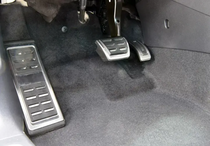 Widok na pedały w samochodzie: sprzęgło, gaz i hamulec. Po lewej pedał podparcia stopy, pośrodku gaz, a po prawej hamulec.