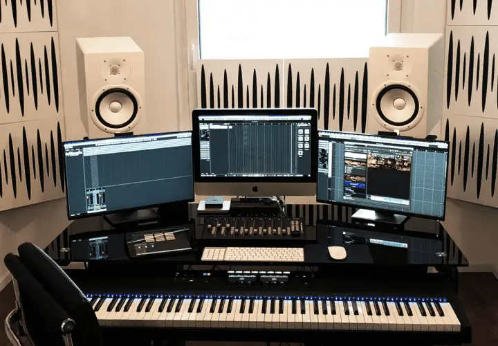Configuration home studio avec trois écrans, enceintes, clavier maître et console de mixage.