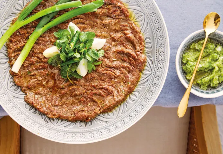 En tallrik med kibbeh nayyeh, rå köttfärs kryddad med bulgur och örter, toppad med vitlök, mynta och chili. Serveras med en grön sås.
