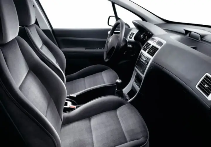 Interior de Peugeot 307, asientos delanteros de tela gris, salpicadero y consola central. Sin anomalia anticontaminacion visible.
