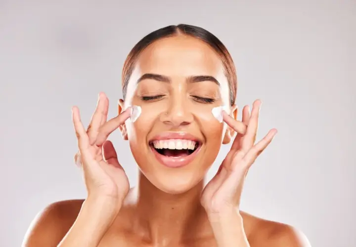 Mujer sonriente aplicándose crema en el rostro. Descubre para qué sirve la niacinamida en la piel y luce radiante.
