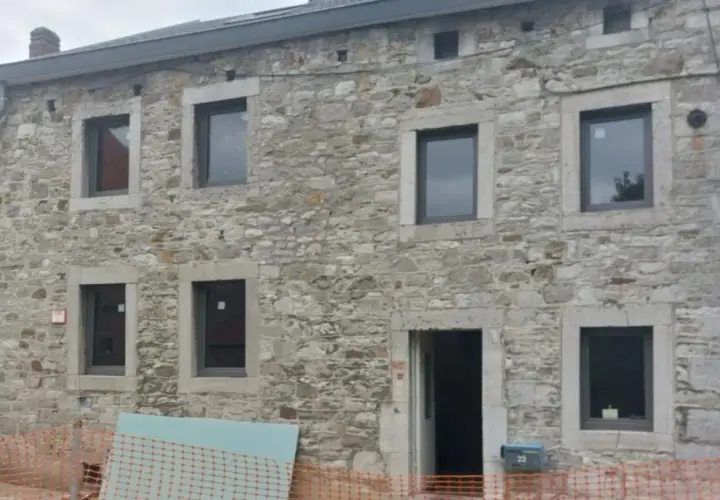 Façade d'une maison en pierre, en cours d'isolation. Fenêtres neuves et entrée ouverte sur un chantier.