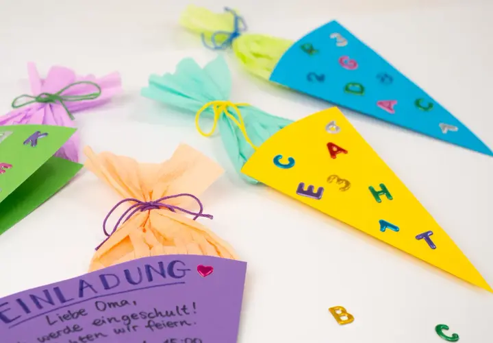 Bunte Schultüten und eine Einladung zum Einschulungsfest basteln. Kleine Buchstaben und Zahlen zieren die Tüten.