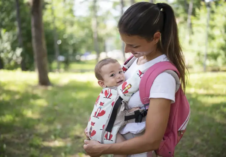 Uśmiechnięta mama z niemowlakiem w nosidełku z lisami. Fizjoterapeuta poleciłby takie, bo wspiera prawidłowy rozwój malucha.