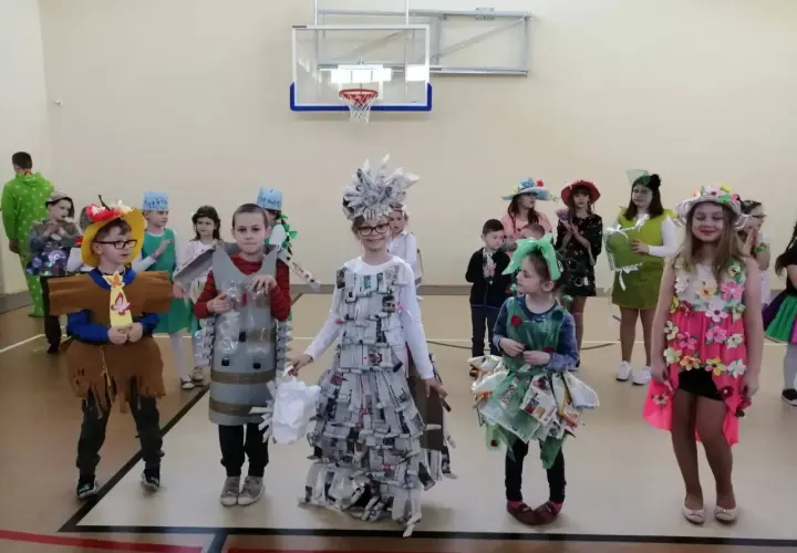 Dzieci prezentują stroje na Dzień Wiosny. Chłopiec w brązowym stroju z frędzlami, obok niego chłopiec w stroju z butelek.