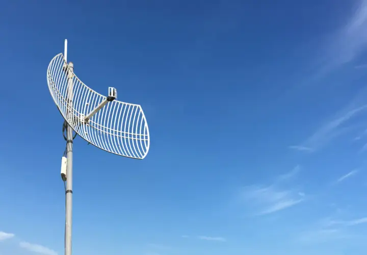 Siatkowa antena telewizyjna na tle błękitnego nieba z chmurami.