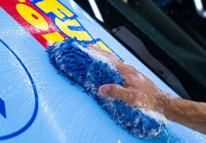 Mano con spugna blu insaponata mentre si lava un'auto con adesivi gialli e rossi.
