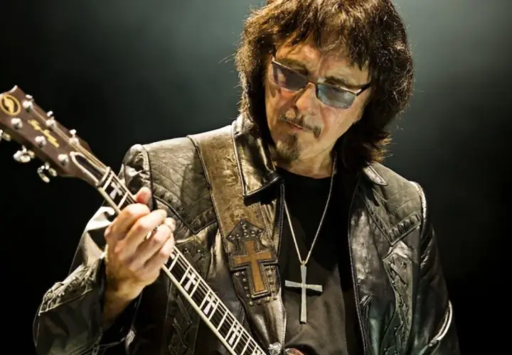 Tony Iommi fingers grają na gitarze, w okularach i skórzanej kurtce z krzyżem.