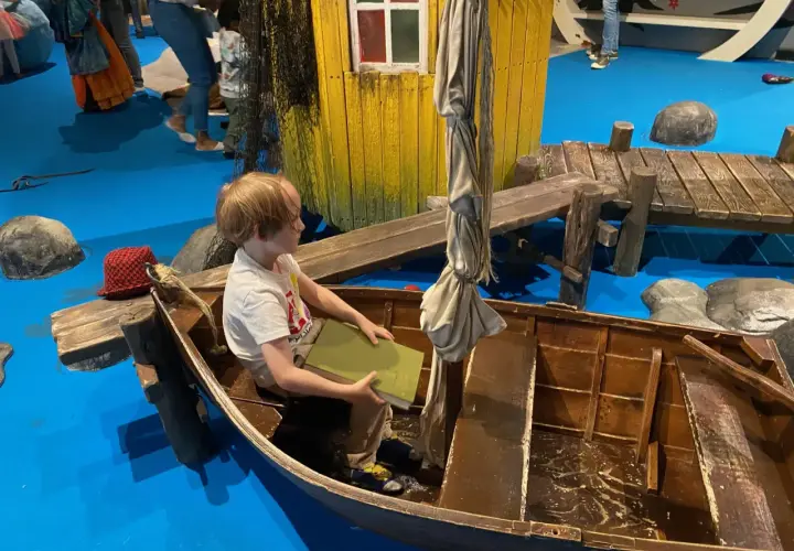 Un bambino legge un libro in una barca, un'installazione interattiva che ricorda Stoccolma con bambini.