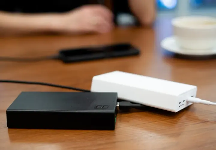 Dwa powerbanki, czarny i biały, leżą na drewnianym stole. W tle widać dłonie i filiżankę kawy. To idealny moment na sprawdzenie powerbank ranking.