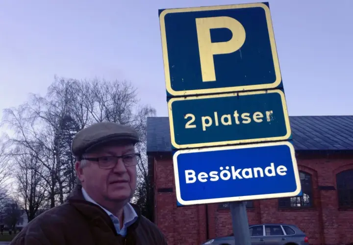 Man i keps vid parkering för personbil klass 2. Skylten visar "2 platser Besökande".